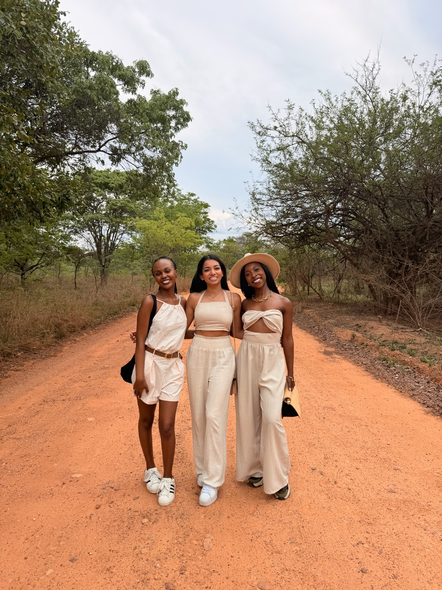 Three travellers standing together on a red dirt road surrounded by trees